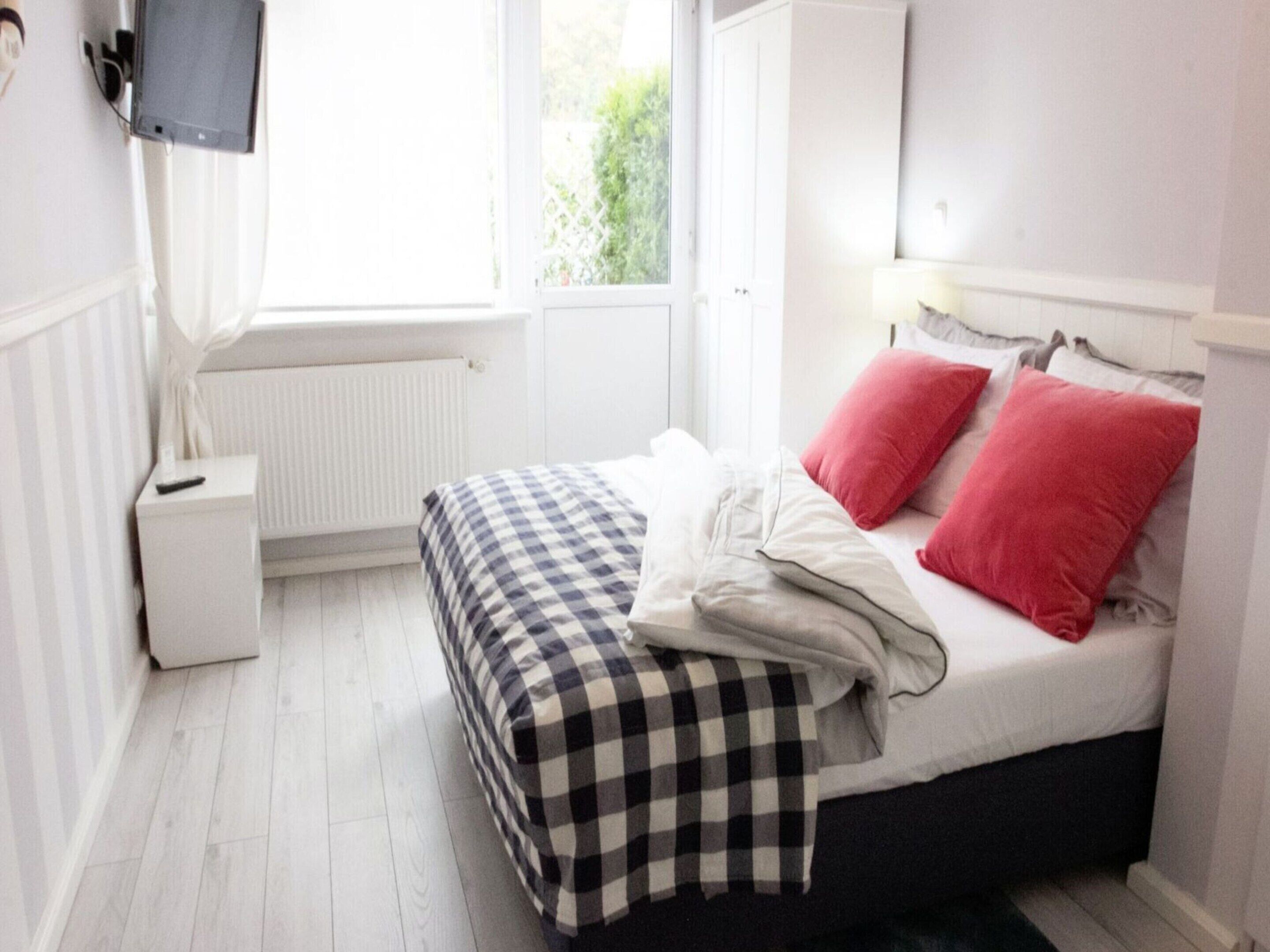Un dormitorio con cama, mesita de noche, televisor y ventana con vista a la vegetación.