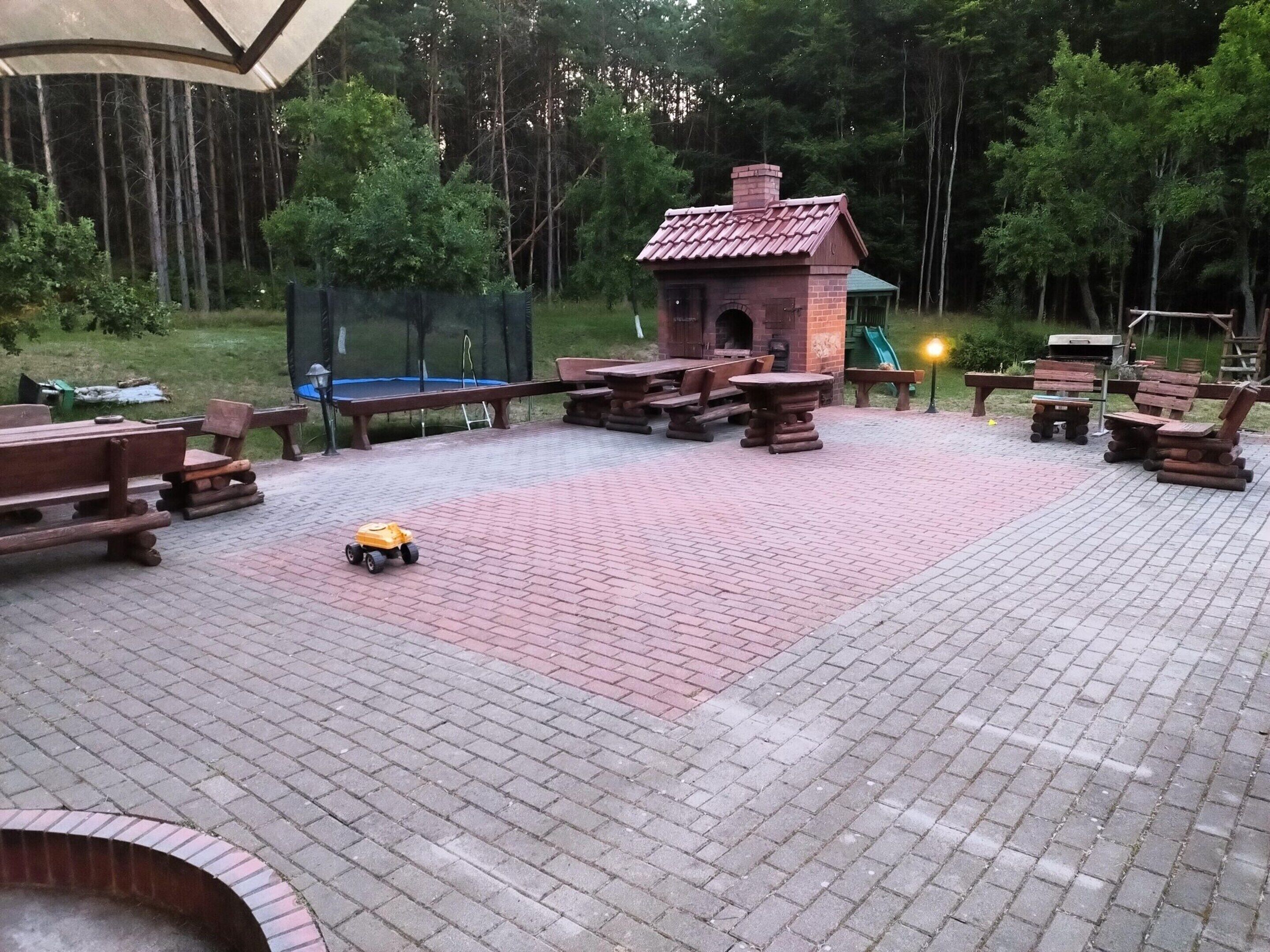 Un patio con suelo de ladrillo, bancos de madera, mesas de picnic y una pequeña construcción de ladrillo.
