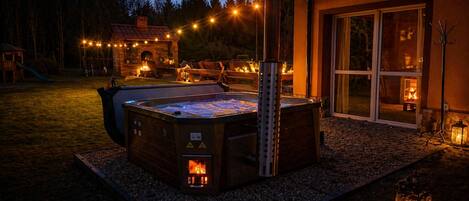 A hot tub with a fire feature, surrounded by a patio area with outdoor lighting and a stone pathway.