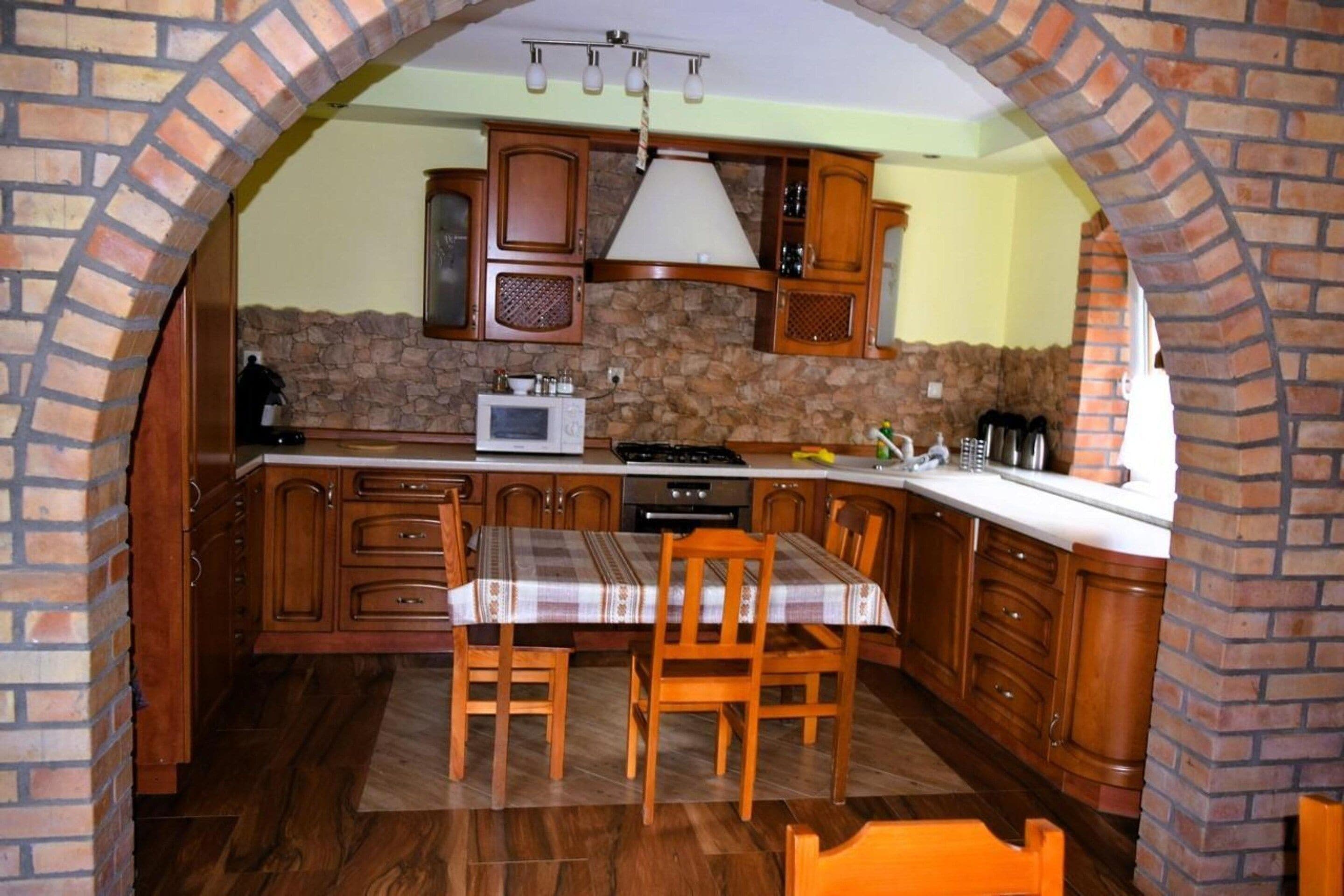 Una cocina con pared de piedra, armarios de madera, microondas y una mesa de comedor con sillas.