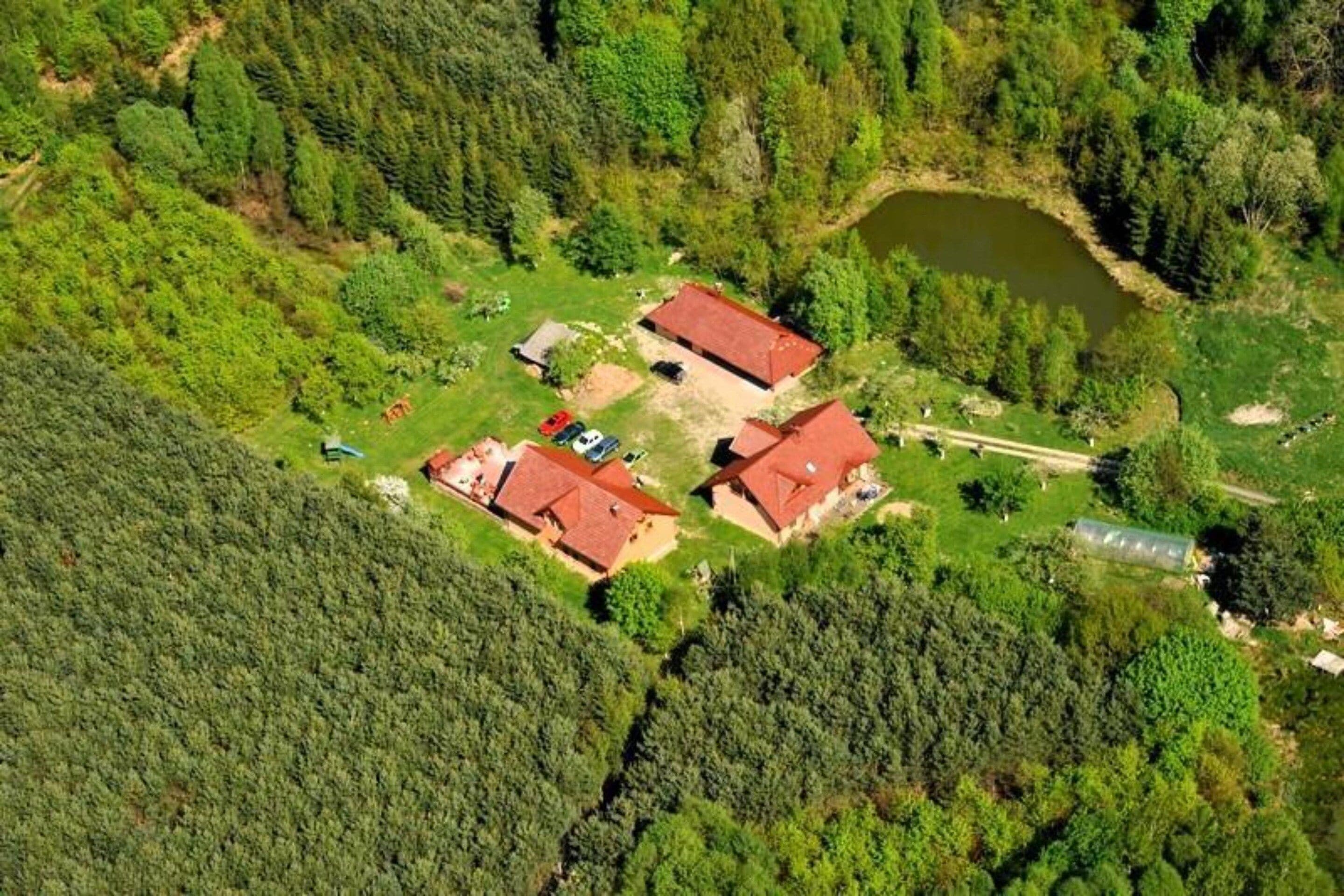 Propiedad campestre con dos edificios principales, un estanque y bosque denso.