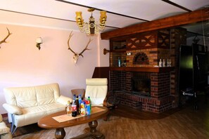 A living room with a brick fireplace, a sofa, a coffee table with drinks, and a chandelier. - Holiday Home in Natura 2000 With Fishing (Tuczno)