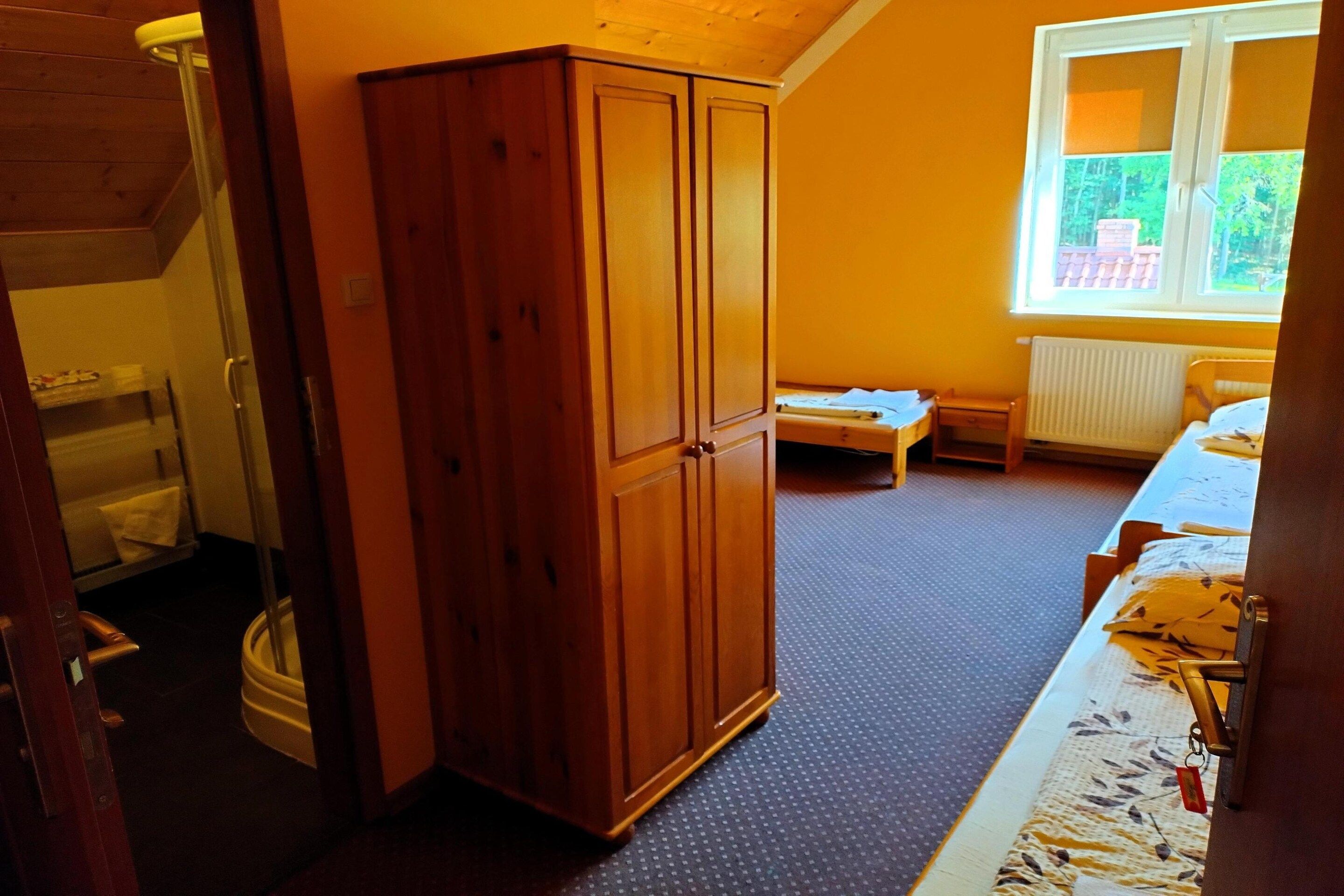 Una habitación con un armario de madera, una mesita, un radiador y una ventana con vistas a zonas verdes.