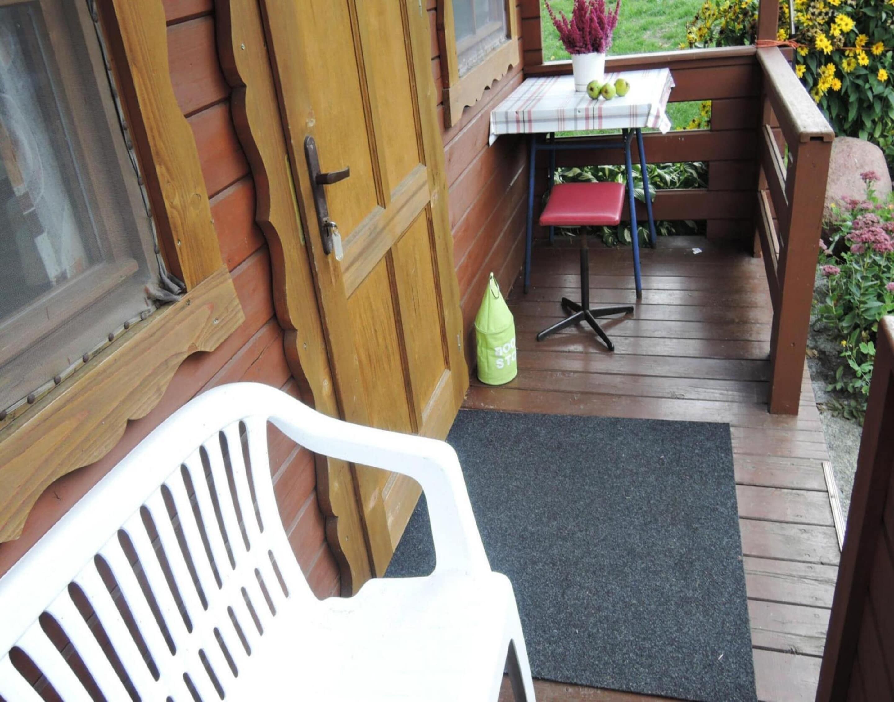 A wooden deck with a table and chairs, a door, and a small garden area with flowers.