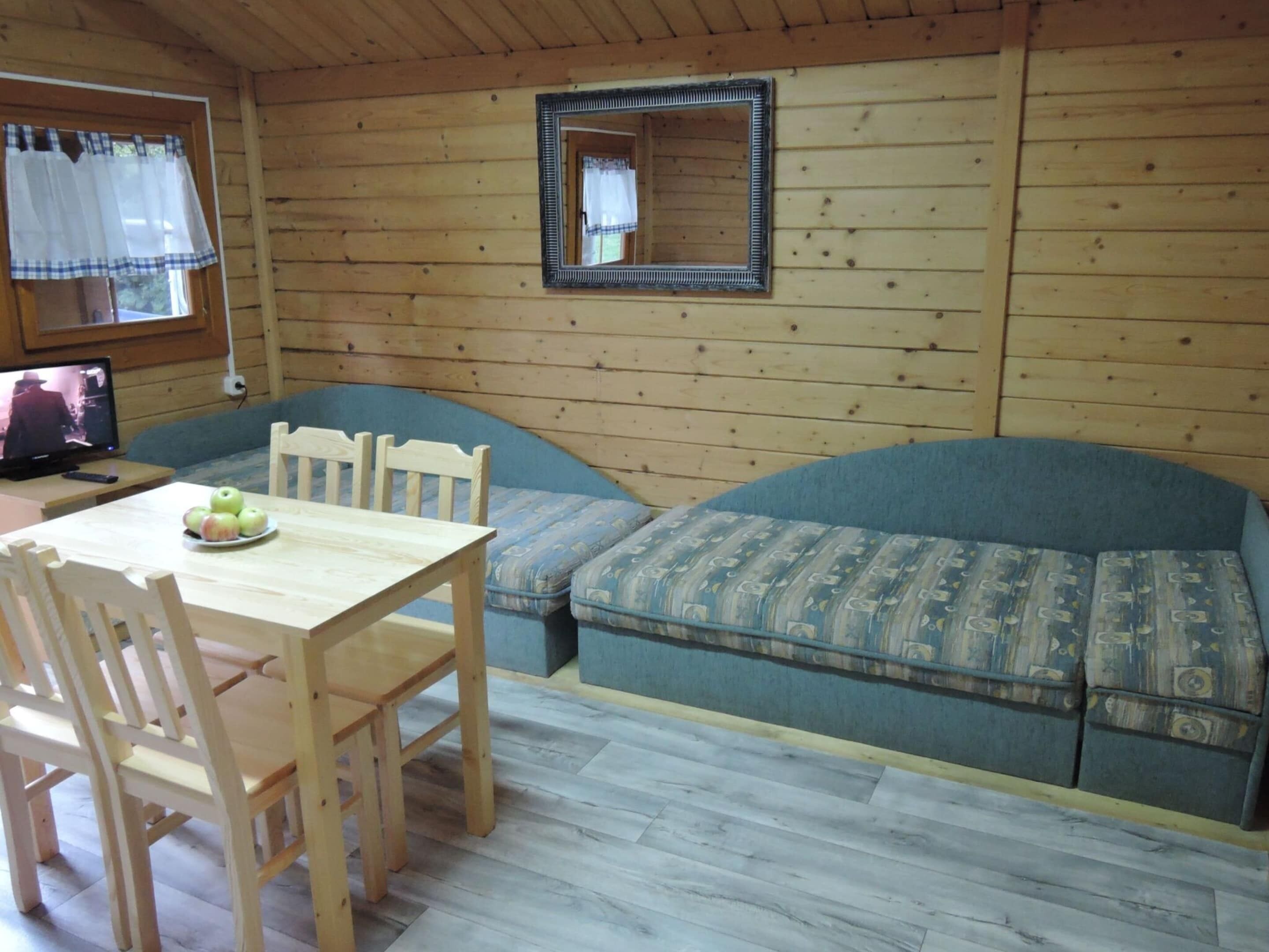 L'intérieur d'un chalet en bois, avec une table à manger, des chaises, un canapé et un téléviseur.