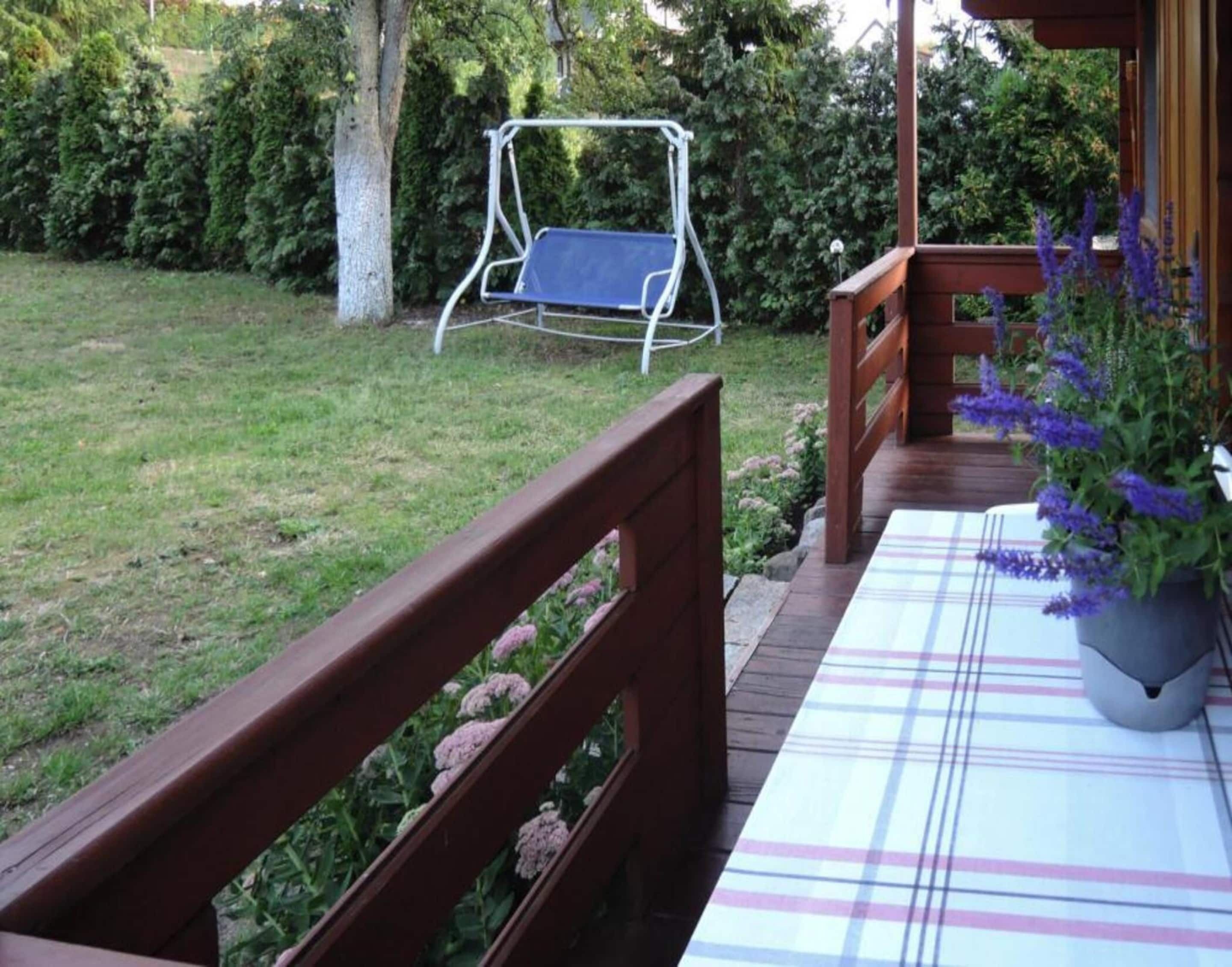 A wooden deck with a plaid tablecloth, a swing, and a potted plant with purple flowers.