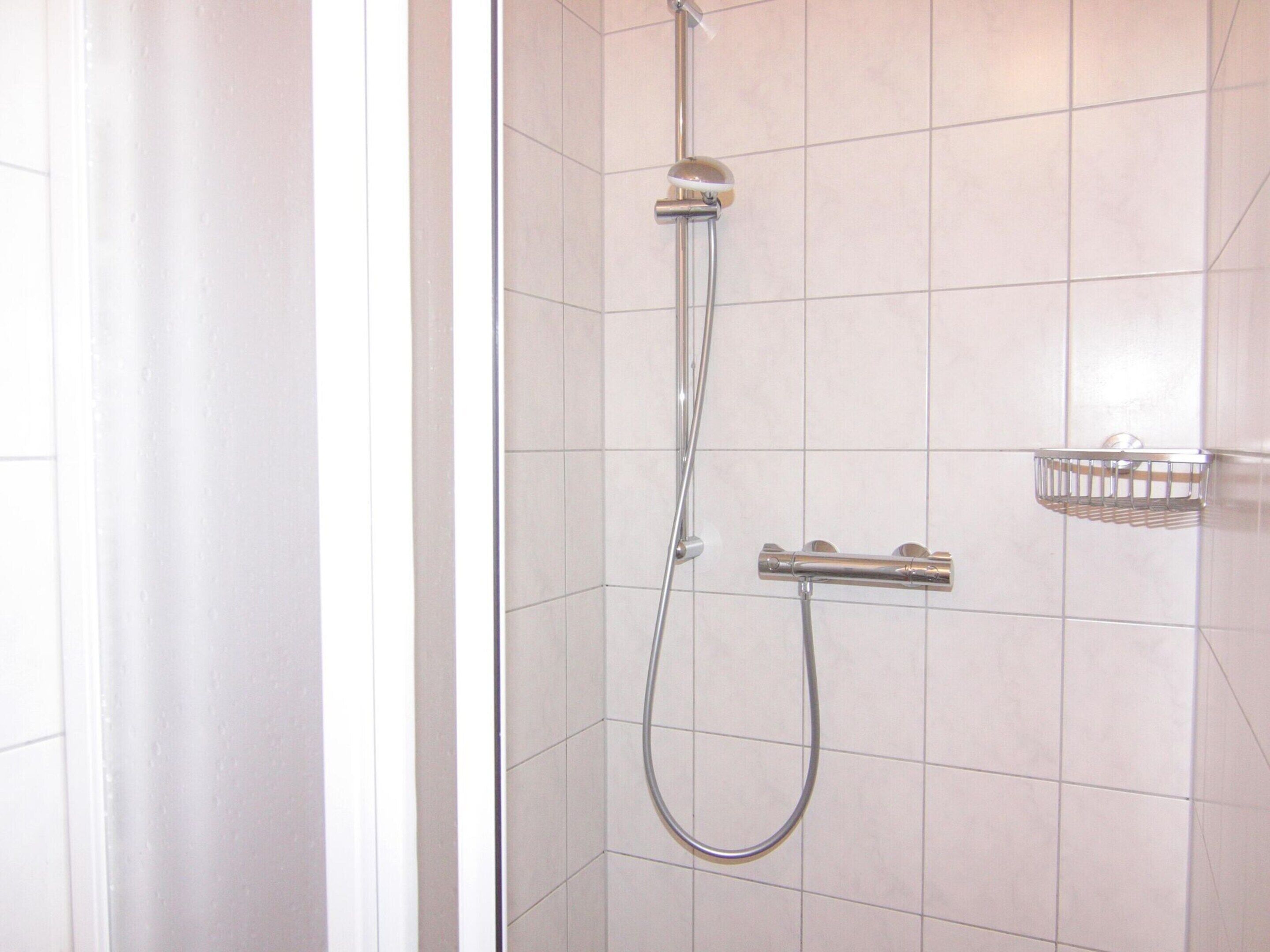 Una ducha con cabezal de ducha manual y grifo empotrado, un panel de control de ducha cromado y un cabezal de ducha cromado.