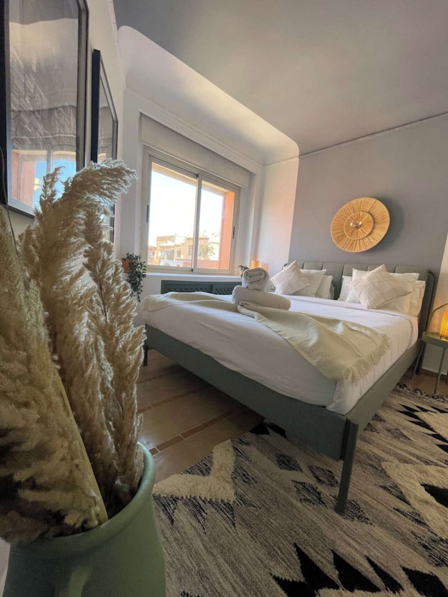 Un dormitorio moderno con cama, ventana, una lámpara circular fijada a la pared y una planta decorativa.