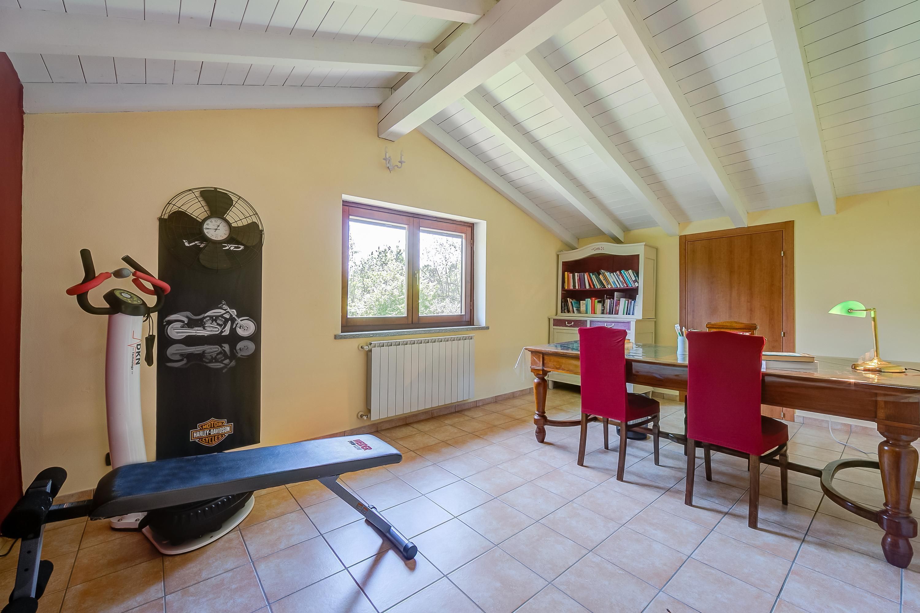 Una habitación con ventilador de techo, ventana, escritorio y sillas, y un radiador.