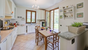 Une cuisine avec des meubles blancs, une table à manger en bois et un lustre.