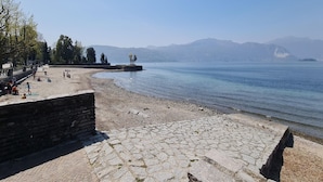 Une promenade dallée de pierres, bordant un lac paisible, avec des montagnes lointaines, des bancs et des arbres.