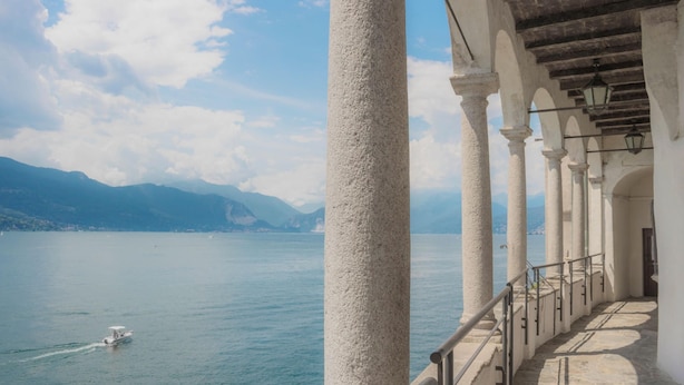 Un bâtiment situé au bord de l’eau, doté de colonnes et d’un balcon donnant sur un lac paisible où se trouve un bateau.