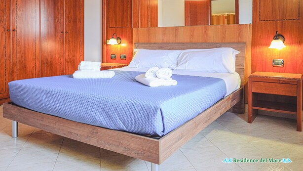 Ein Schlafzimmer mit einem Bettgestell aus Holz, einer blauen Bettdecke, zwei Nachttischen mit Lampen und Holzschränken.