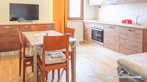 Eine kleine Küche mit Holzausstattung, einem Esstisch mit Stühlen, einem Fernseher und einem Fenster mit Vorhängen.