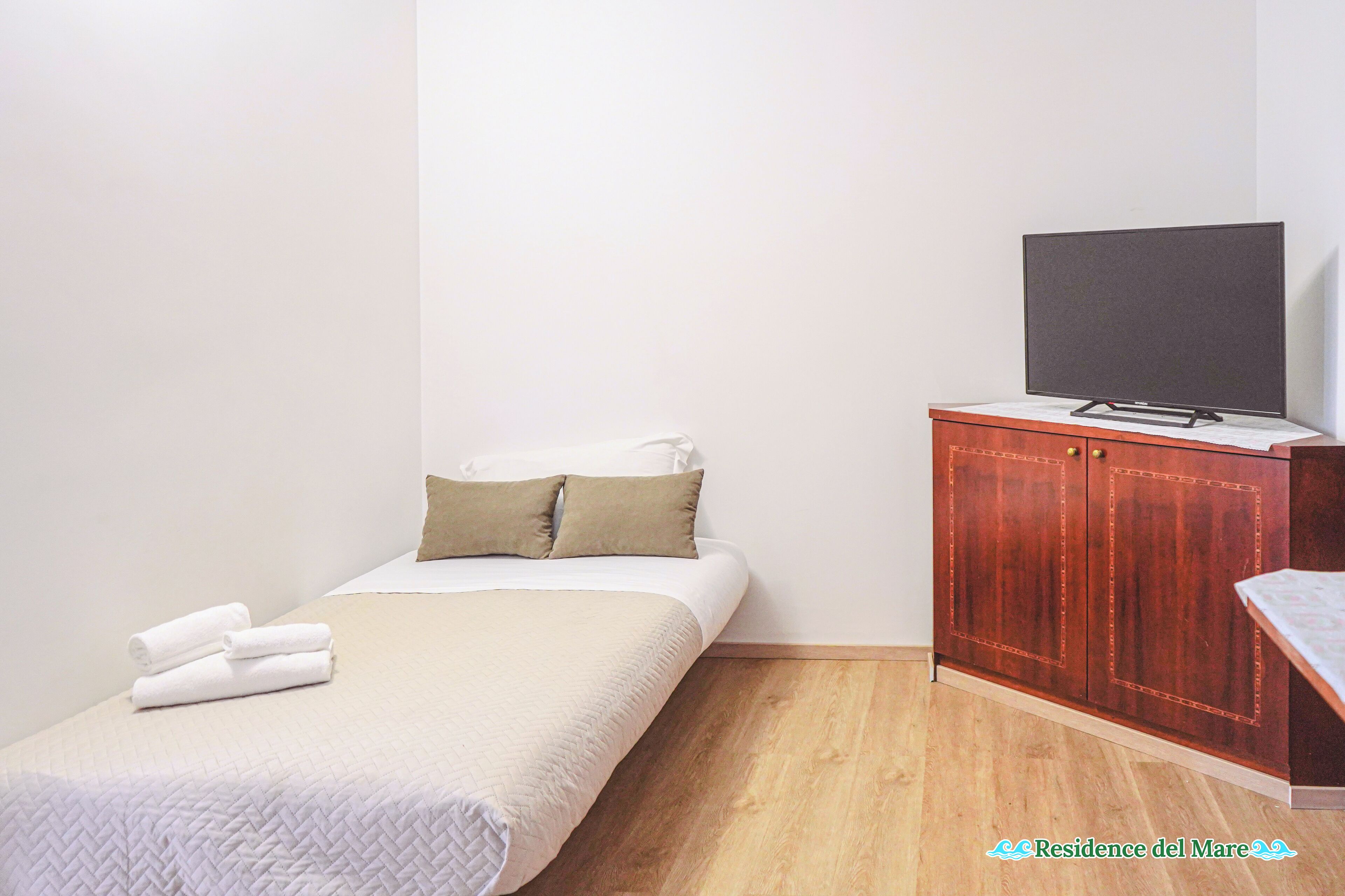 Ein Schlafzimmer mit einem Bett, einem Fernseher auf einer Holzkommode und einem kleinen Tisch.