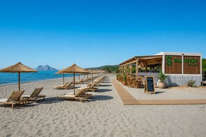 Ein Restaurant direkt am Strand mit Außenbereich, einer Holzterrasse und einem Schild mit Speiseauswahl.