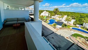 A balcony with a sofa and a small table, overlooking a swimming pool and lush greenery. - Terrazas de Alcaidesa Golf & Beach 2139 (La Alcaidesa)