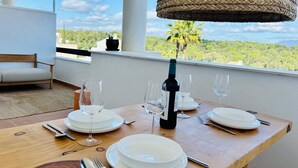 A dining table set for four with plates, glasses, and cutlery, a bottle of wine, and a woven pendant light. - Terrazas de Alcaidesa Golf & Beach 2139 (La Alcaidesa)