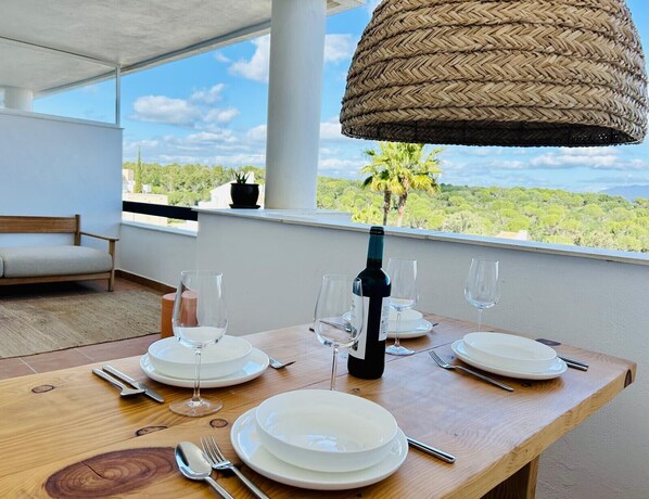 A dining table set for four with plates, glasses, and cutlery, a bottle of wine, and a woven pendant light.