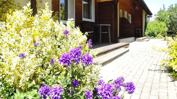 A wooden cabin with a covered porch, outdoor seating, and a garden with purple flowers. - House in Kolczewo Near Baltic Sea & Lake (gmina Wolin)