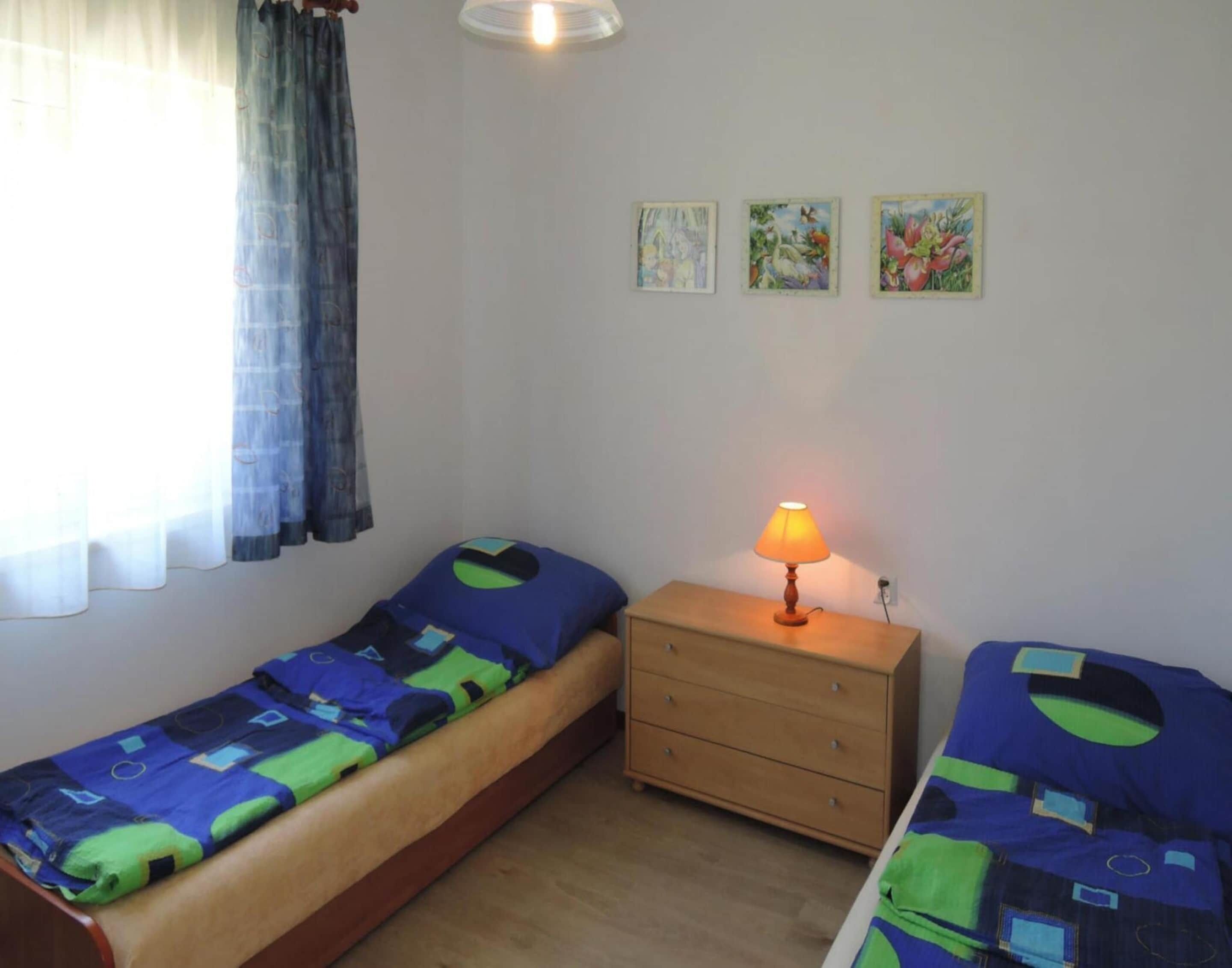 Un alojamiento pequeño y de una sola habitación, con una cama, una mesita de noche con lámpara, y tres cuadros colgados en la pared.