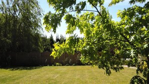 A backyard with a grassy lawn, a wooden fence, and a tree with green leaves. - House in Kolczewo Near Baltic Sea & Lake (gmina Wolin)