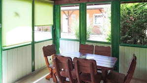 A covered patio with a wooden table and chairs, surrounded by green-painted walls and windows. - House in Kolczewo Near Baltic Sea & Lake (gmina Wolin)