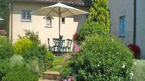A house with a patio, a table with chairs, and a large umbrella. - Apartment in Tuscany With Pool & Golf (Gambassi Terme)