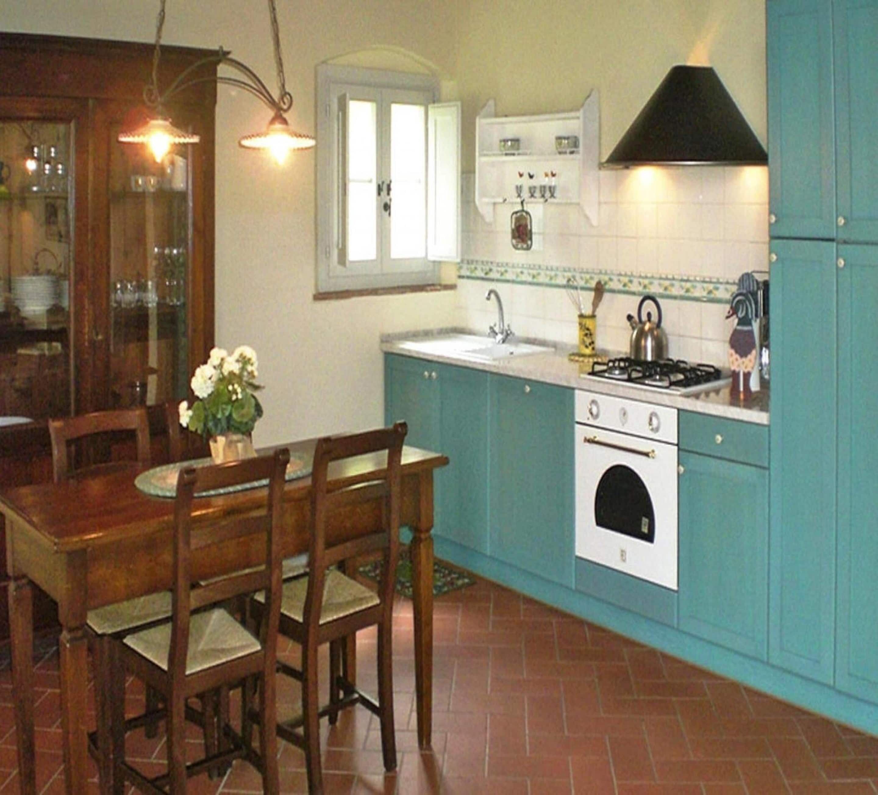 Una cocina con gabinetes azul verdosos, una estufa blanca y una mesa de comedor con sillas.