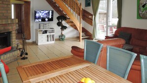 A living room with a wooden table, a sofa, a TV, a staircase, and a potted plant. - Holiday Home in Nowe Warpno Jagoda (Nowe Warpno)