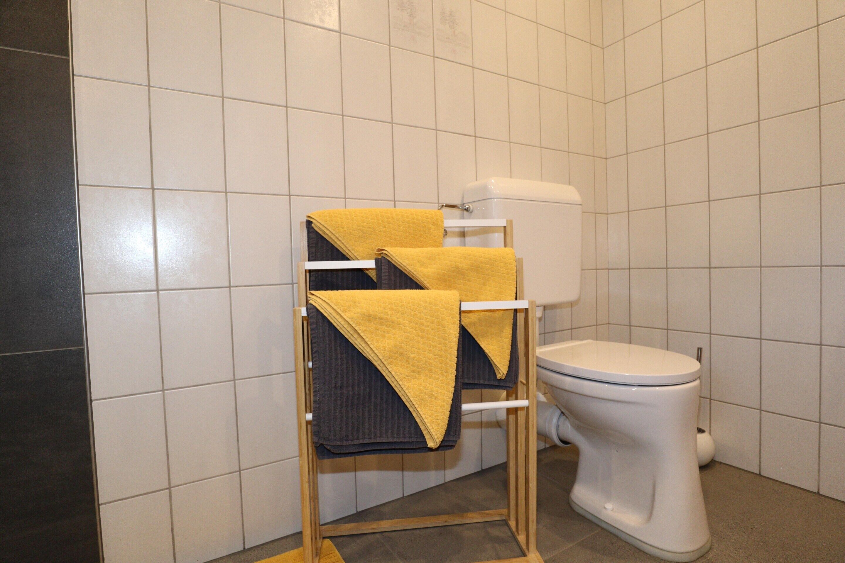 A bathroom with a white toilet, a towel rack with two towels, and a tiled wall.