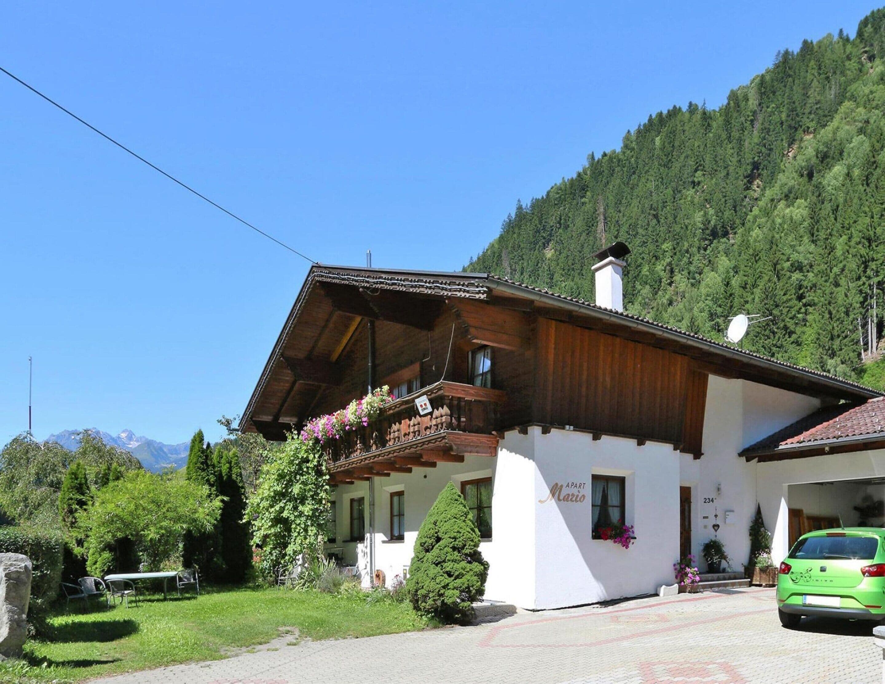 A two-story wooden house with a balcony, a garage, and a mountain backdrop.