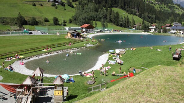 A lakeside resort with a swimming area, a small dock, and a playground. - Apartments Home Mario, See im Paznauntal (See)