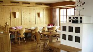 Un intérieur en bois avec plusieurs tables et chaises, un meuble blanc orné de découpes carrées noires et une fenêtre donnant sur l’extérieur.