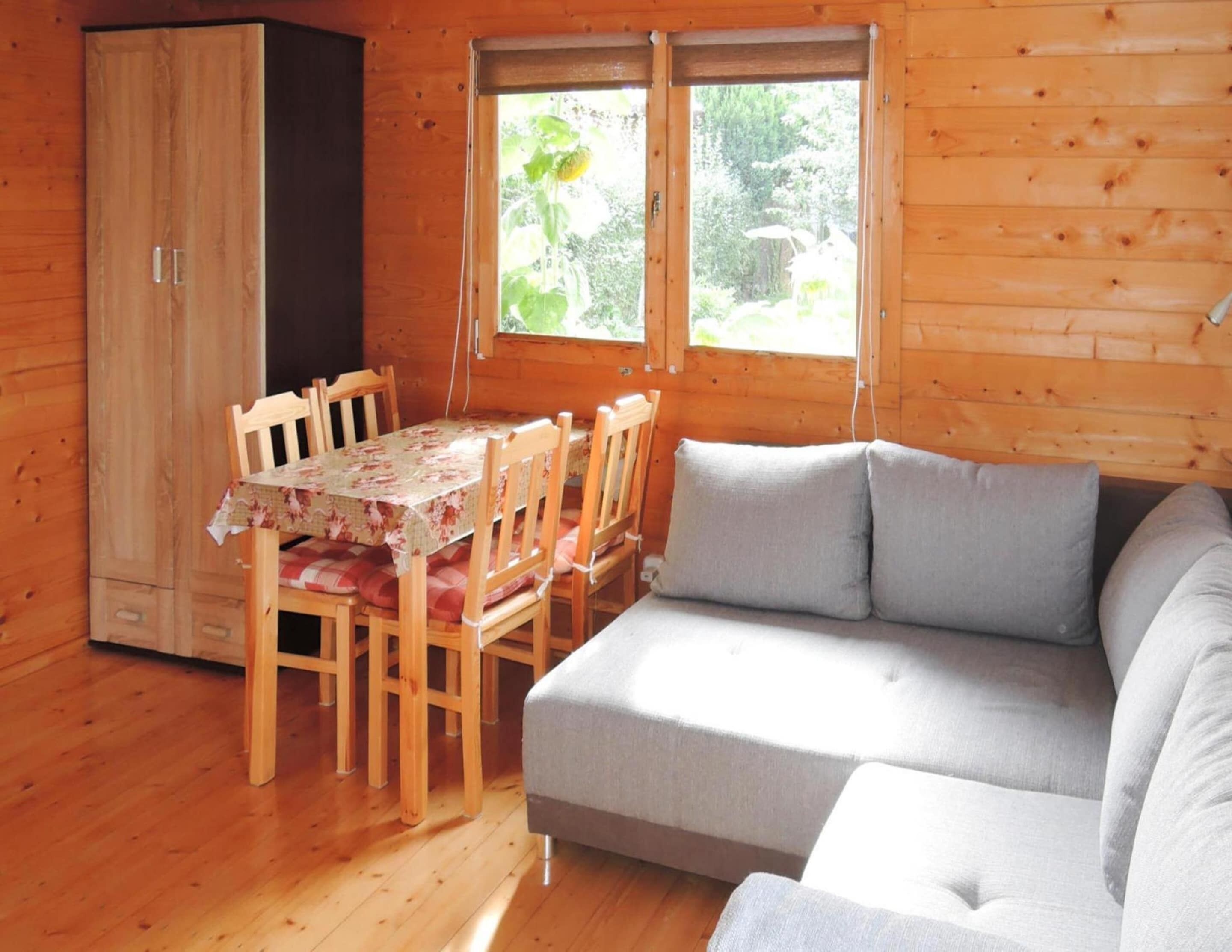 Interior acolhedor de uma cabana com uma mesa de jantar de madeira, cadeiras, um sofá e um guarda-roupa.