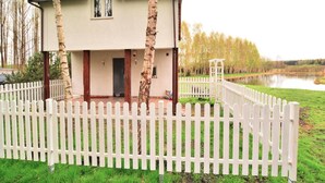 Un bâtiment à deux étages, avec une clôture blanche en bois, un petit porche et une vue sur un lac.
