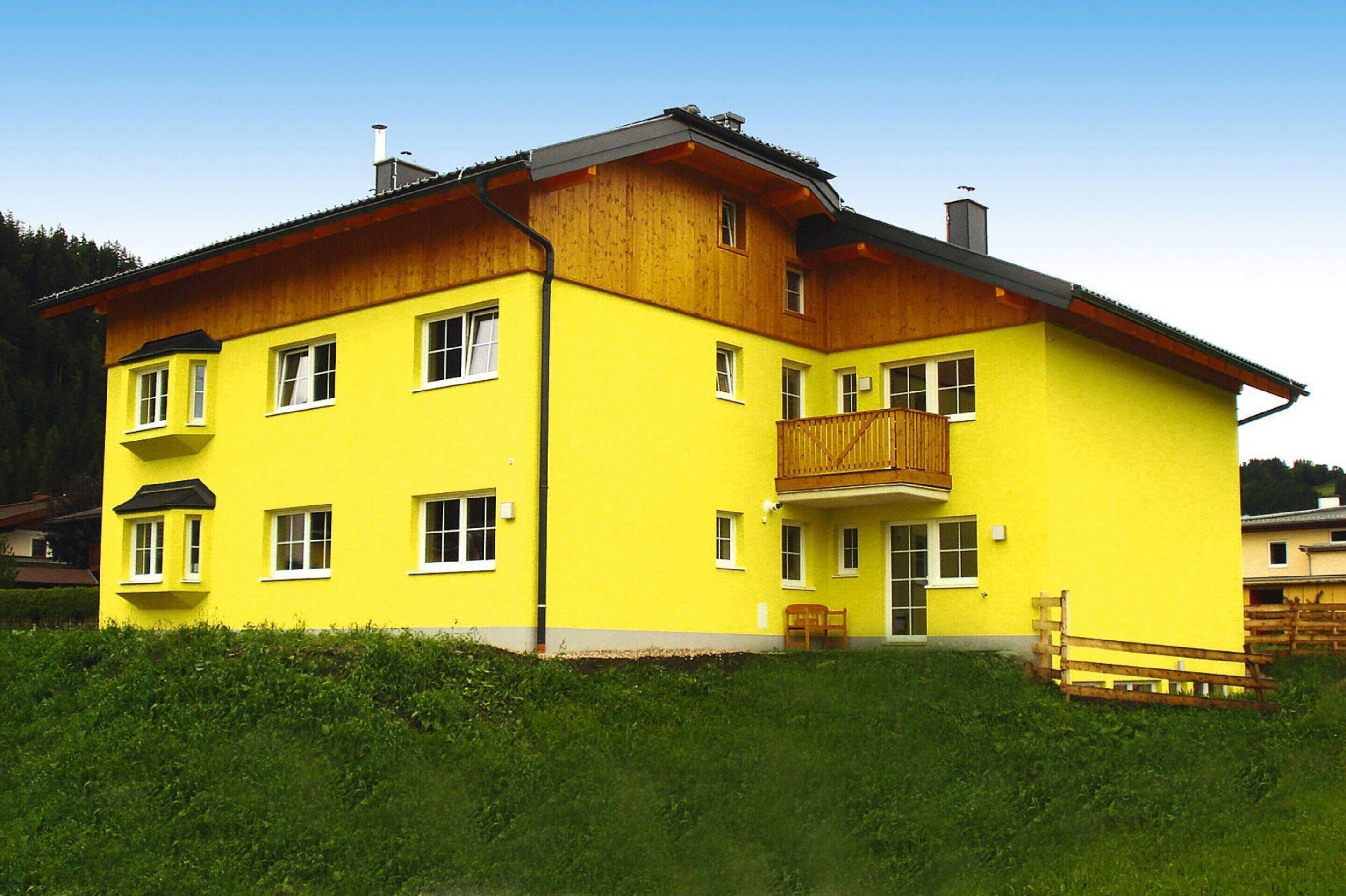 A two-story yellow building with a wooden balcony, multiple windows, and a front door.
