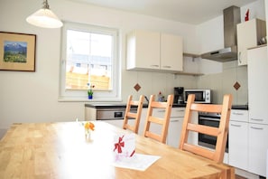 A modern kitchen with white cabinets, a wooden dining table, and a window with a view of buildings.