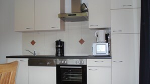 Una cocina compacta con armarios blancos, horno empotrado, cafetera y microondas.