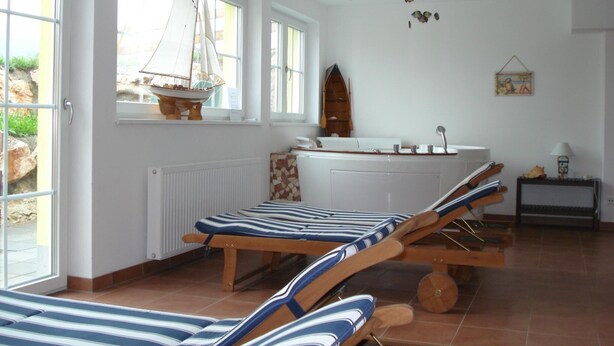 Una habitación iluminada por el sol, con un gran ventanal, un modelo de velero, un bote de madera, una bañera y una mesita con una lámpara.