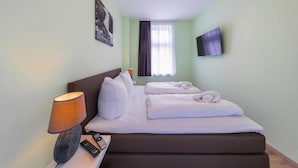 Camera d'albergo con un letto, una TV fissata al muro, una lampada e un quadro appeso alla parete.