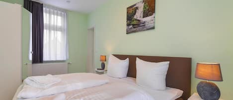 A hotel room with a bed, a nightstand, a lamp, a painting, and a window with curtains.