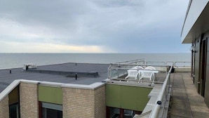 A rooftop terrace with a view of the sea, a covered seating area, and a building with a brick facade. - Wohnung in der Nordseeregion in Strandnhhe (Wyk auf Foehr)