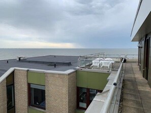 Una terraza en la azotea con vistas al mar, una zona de estar cubierta y un edificio de fachada de ladrillo.