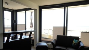 A modern living room with a balcony, a dining area, and large windows. - Wohnung in der Nordseeregion in Strandnhhe (Wyk auf Foehr)