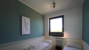 A bedroom with two single beds, a radiator, a window, and a framed picture on the wall. - Wohnung in der Nordseeregion in Strandnhhe (Wyk auf Foehr)