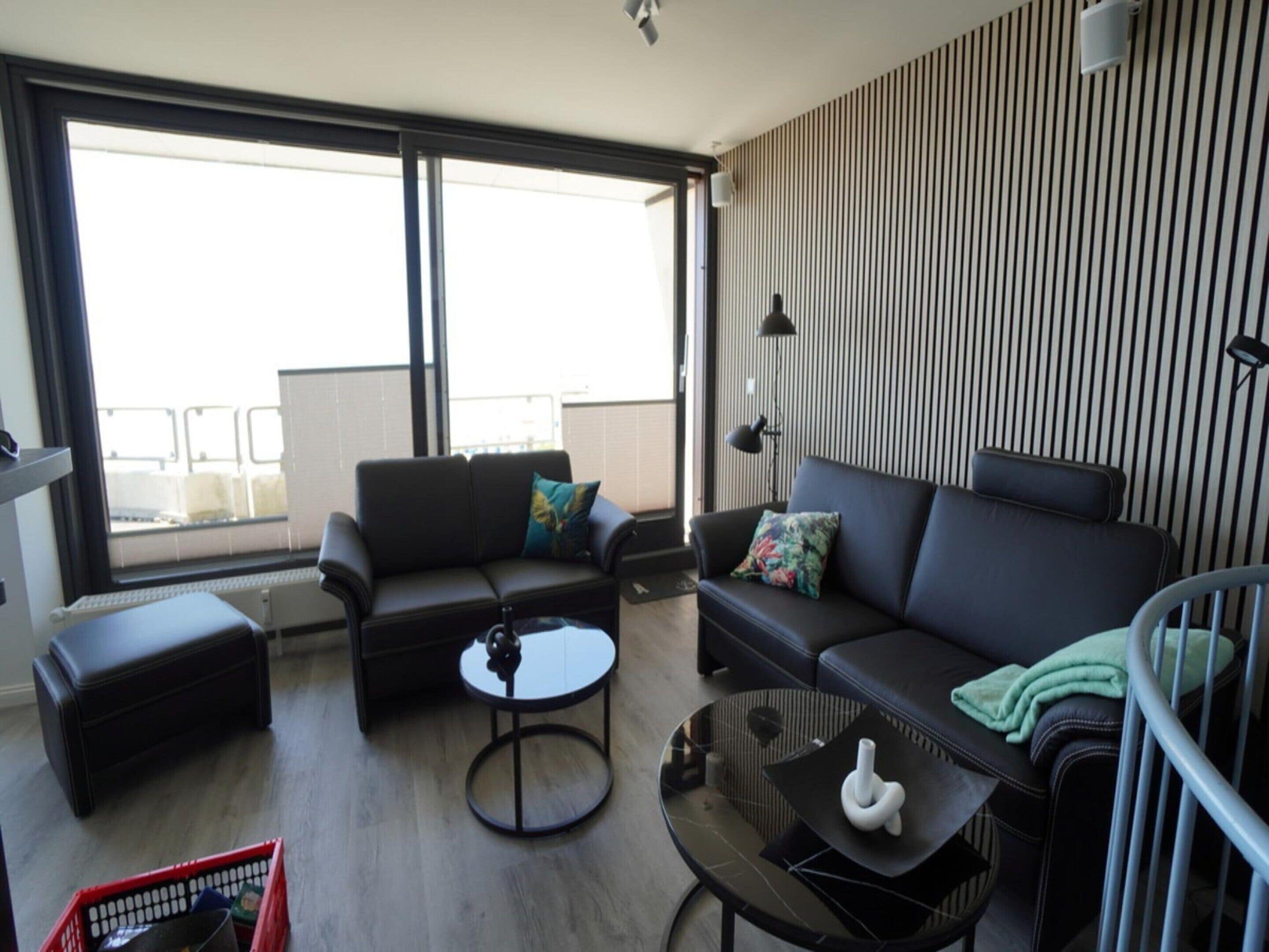A modern living room with a sofa, a coffee table, and a small side table. There is a window providing a view of the outside.