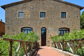 A stone building with a central arched entrance, two windows on the upper floor, and a wooden walkway leading to the entrance. - Apartment in Campiglia Marittima (Campiglia Marittima)