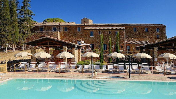 A pool area with lounge chairs and umbrellas, a stone building in the background, and a clear blue sky. - Apartment in Campiglia Marittima (Campiglia Marittima)