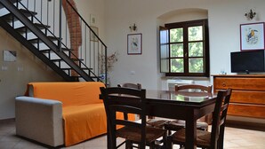 A dining area with a wooden table, chairs, and a sofa. A staircase with a metal railing is visible in the background. - Apartment in Campiglia Marittima (Campiglia Marittima)